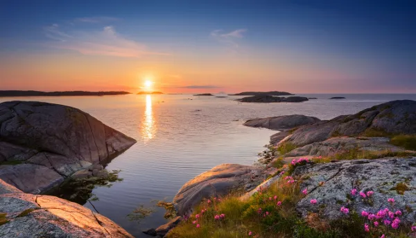 Alt-text: Solnedgång över Bohusläns klippkust med rosa strandtrift, släta granithällar och lugnt hav i skärgården.