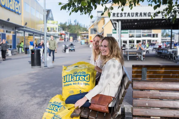 Två kvinnor med shoppingkassar från Gekås Ullared sitter på en bänk utanför varuhuset och tar en paus efter shoppingrundan.