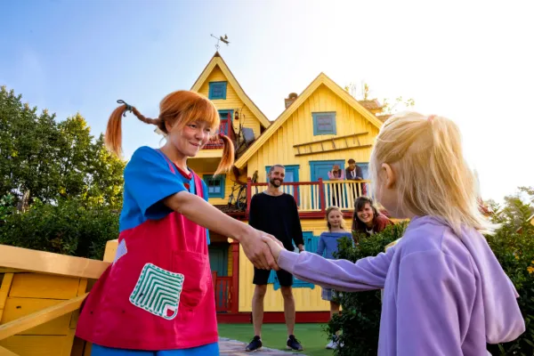 Barn möter Pippi Långstrump utanför Villa Villekulla i Astrid Lindgrens Värld medan familjer tittar på.