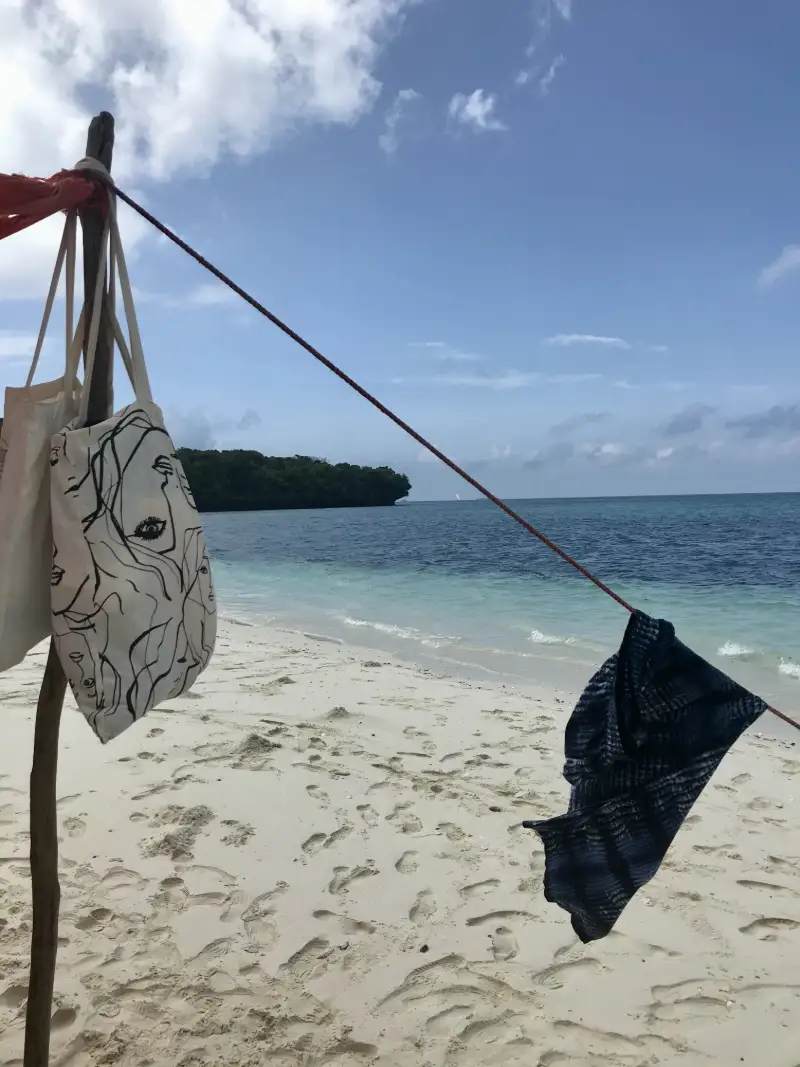 Strandvy med turkost hav och strandväskor upphängda i skuggan på Zanzibar