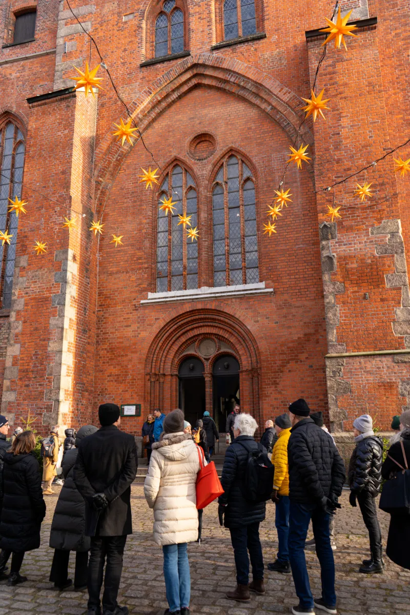 Besökare utanför tegelkyrka dekorerad med julstjärnor på julmarknad i Lübeck