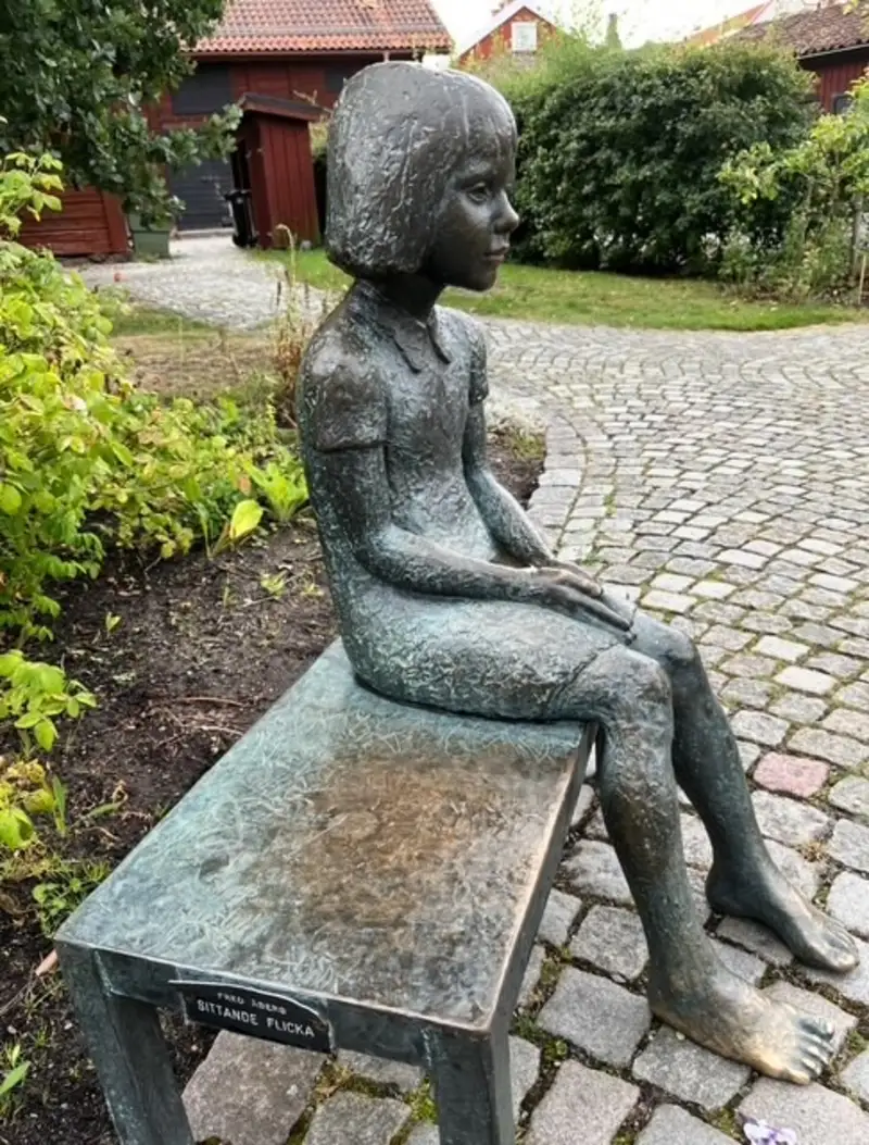 Bronsstaty av sittande flicka i idyllisk parkmiljö i Sverige