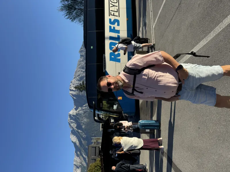 *Resenär framför Rolfs Flyg & Buss-buss med bergslandskap i bakgrunden