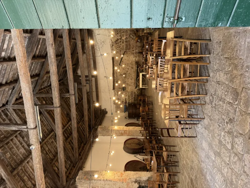 Rustik restaurangmiljö med träbjälkar, sten golv och uppdukade bord med ljusslingor i taket