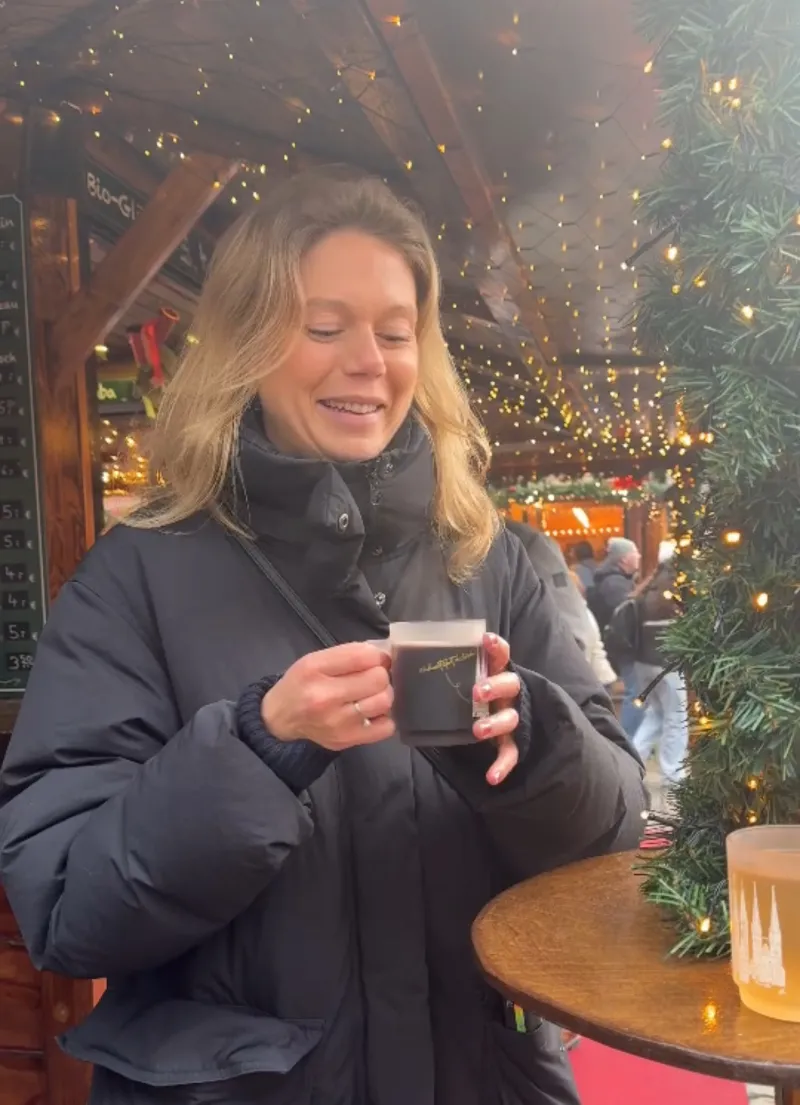 Kvinna med varm dryck på julmarknad bland julbelysning