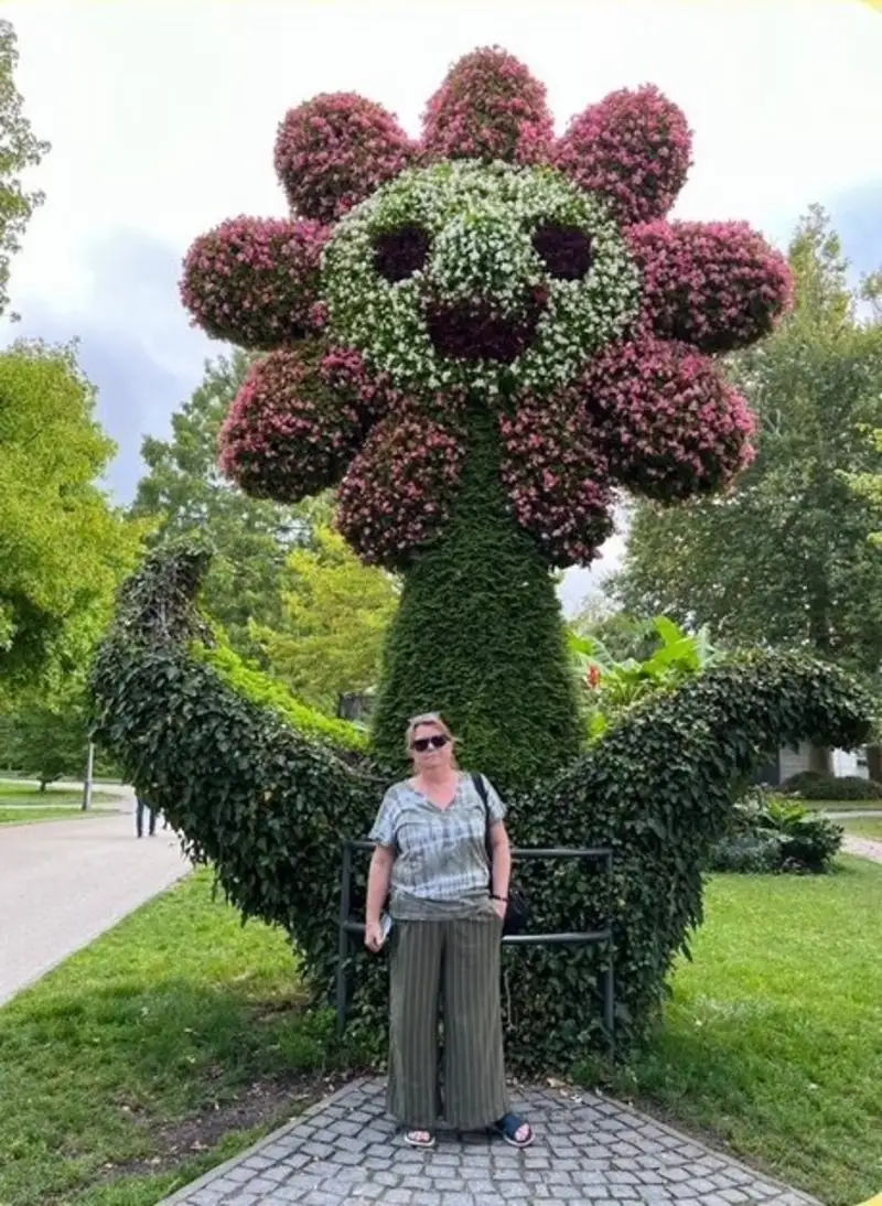Person poserar framför stor blomsterskulptur formad som en blomma i park