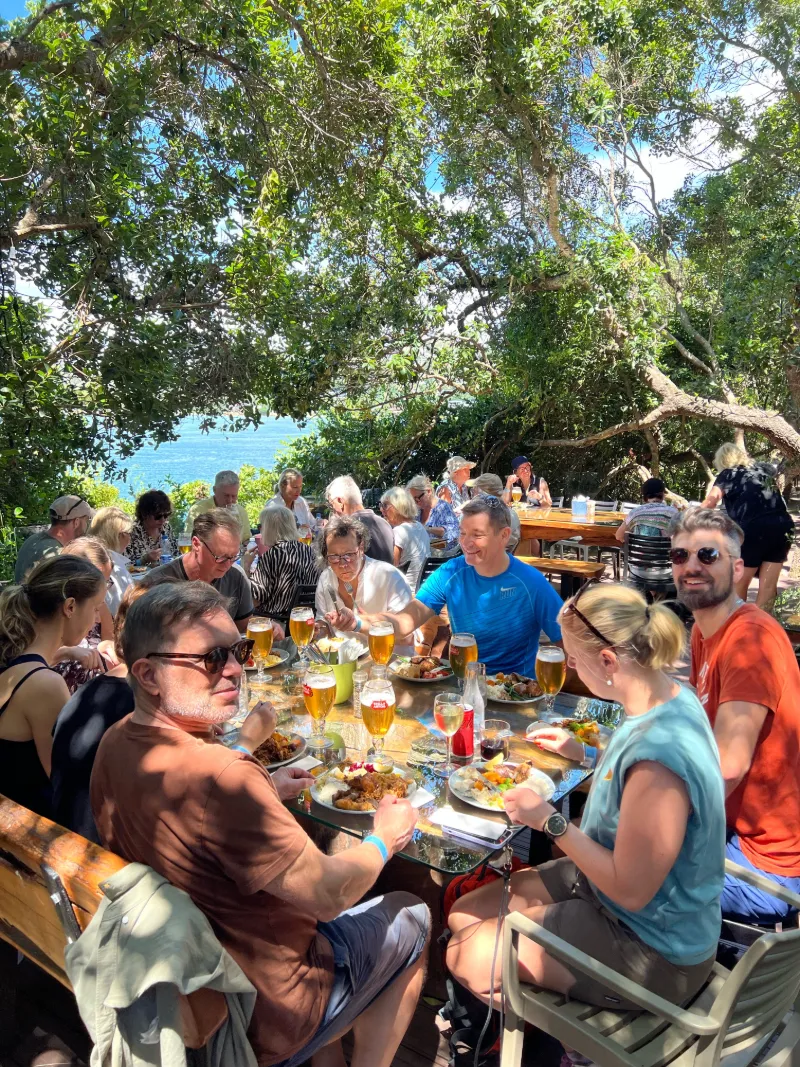 Resesällskap njuter av lunch utomhus i skuggig miljö vid havet under safariresa