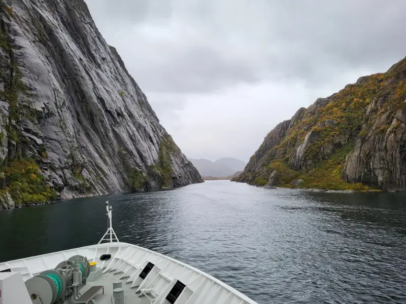 Kryssningsfartyg genom smal fjord med branta klippor och dramatiskt landskap i Norge