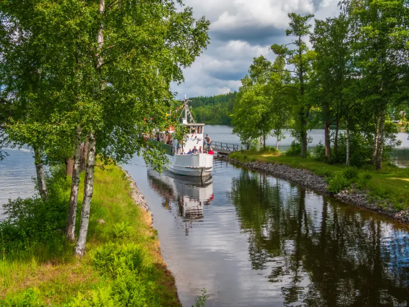 Passagerarbåt på Dalslands kanal omgiven av grönskande skog, lugnt vatten och natursköna omgivningar.