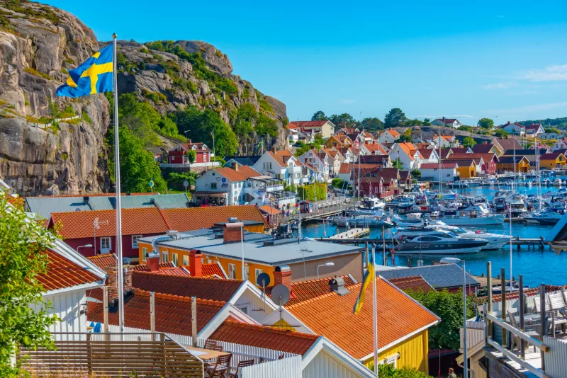 Fjällbacka kustby med småbåtshamn, röda sjöbodar och svenska flaggor vid Bohusläns klippiga kust.