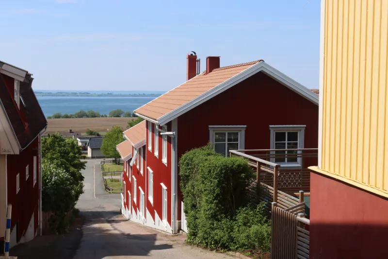 Röda trähus i Gränna längs en lugn gata med utsikt över havet och det öppna landskapet i bakgrunden.
