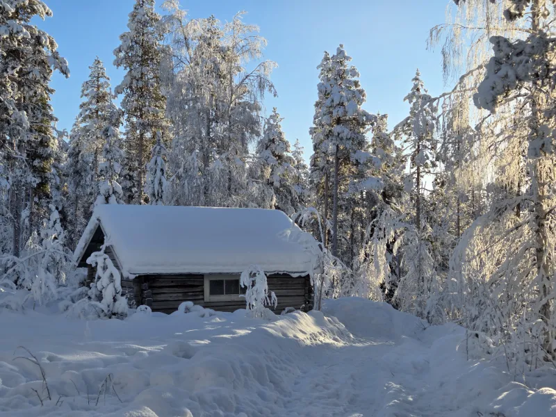 Snötäckt stuga och vinterlandskap i norra Sverige