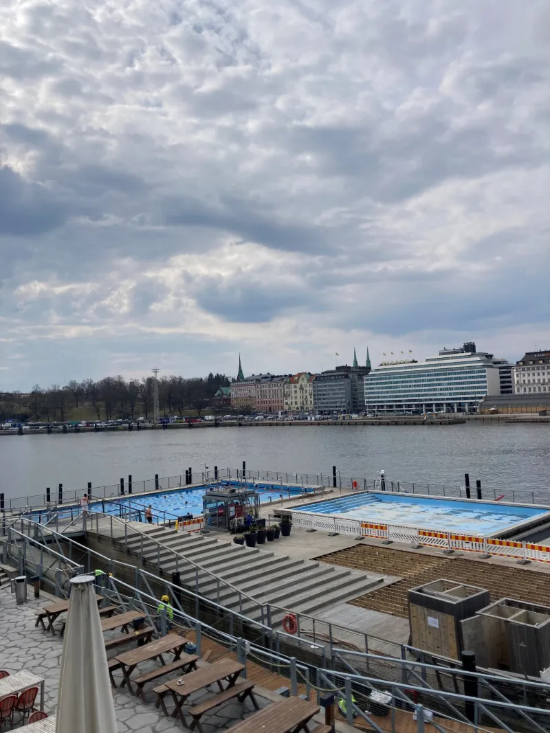Vårvy över Helsingfors hamn och strandpromenad under dramatisk himmel