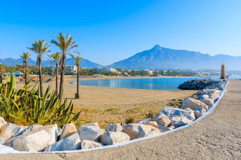 Strandpromenad i Marbella med palmer, hav och berg i bakgrunden