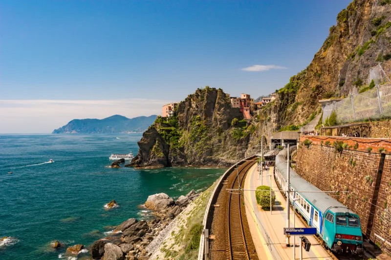 Tåg som färdas längs den dramatiska kusten i Cinque Terre med havsutsikt och klippbyar i Ligurien.