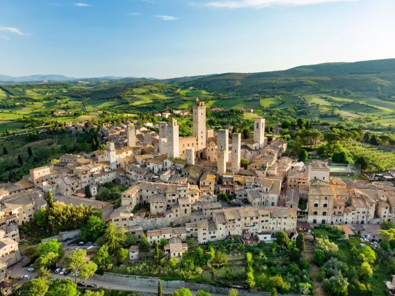 Flygvy över San Gimignano med sina medeltida torn omgiven av Toscanas gröna landskap.