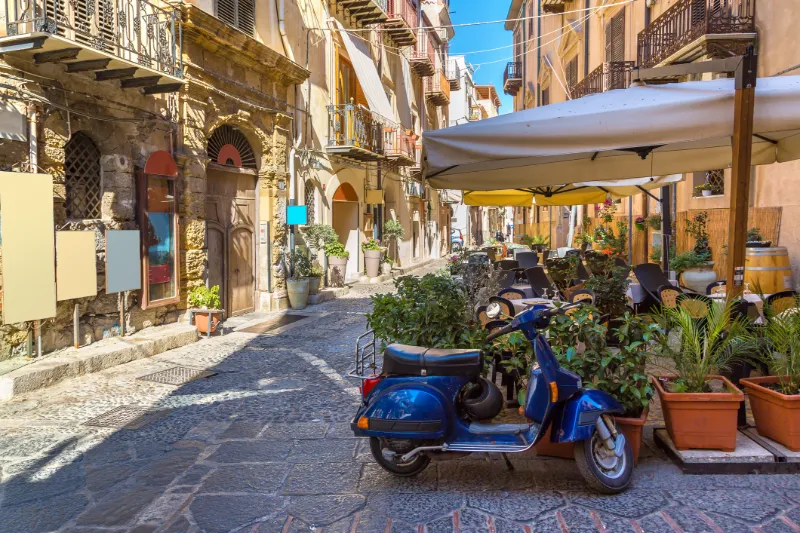 Smal gränd i Sicilien med historiska byggnader och blå vespa