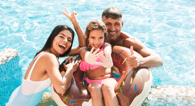 Glad familj som leker tillsammans i en solig hotellpool.