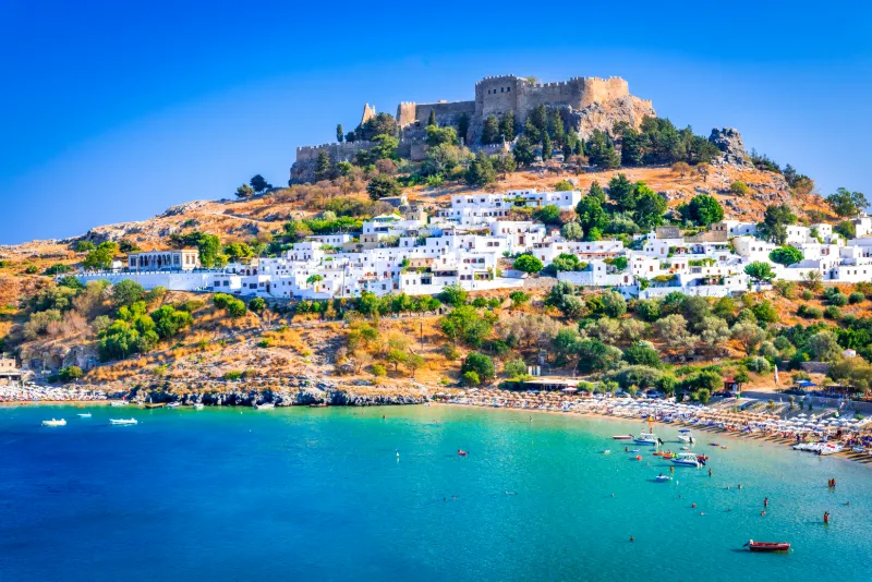 Vy över Lindos på Rhodos med vitkalkade hus som klättrar uppför sluttningen mot den medeltida borgen på höjden.