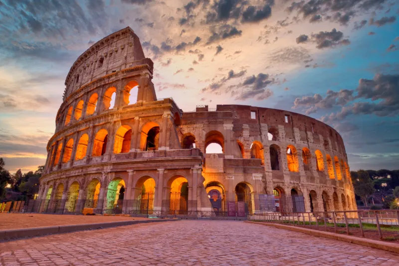 Colosseum i Rom upplyst i kvällsljus under en dramatisk himmel.