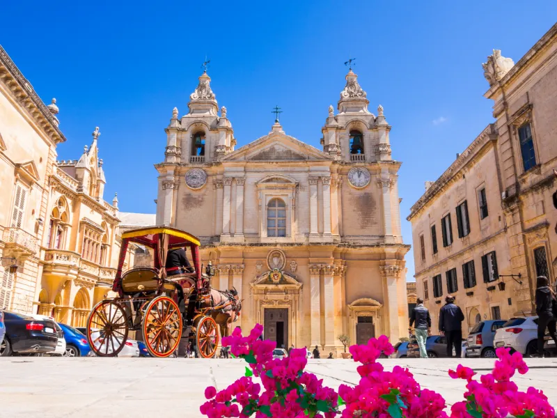 Barockkatedral på ett soligt torg i Mdina på Malta, omgiven av historiska stenbyggnader.