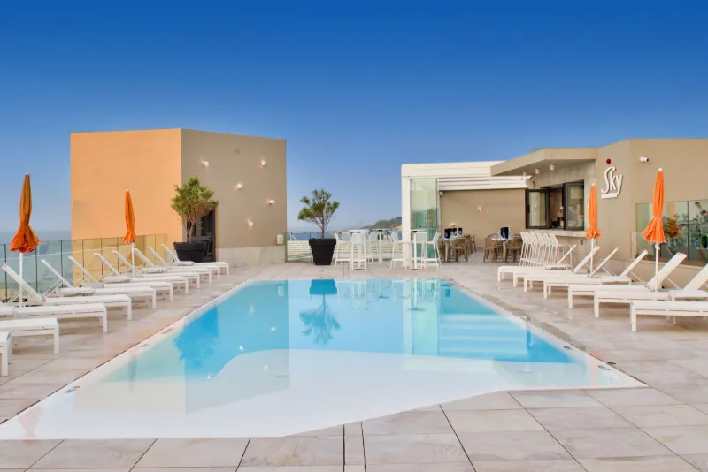 Modern takterrass med pool, vita solstolar och orange parasoller framför en elegant bar och lounge.