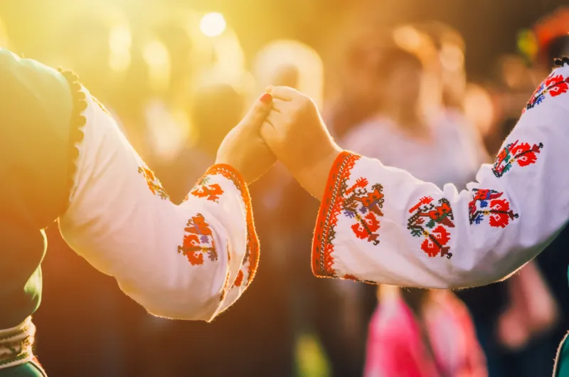 Personer i traditionella bulgariska folkdräkter håller varandra i händerna under en folkdans i kvällssolen