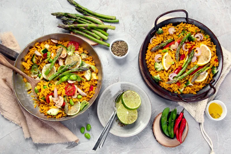 Två skålar med färgstark paella och färska grönsaker serverade på ett bord.